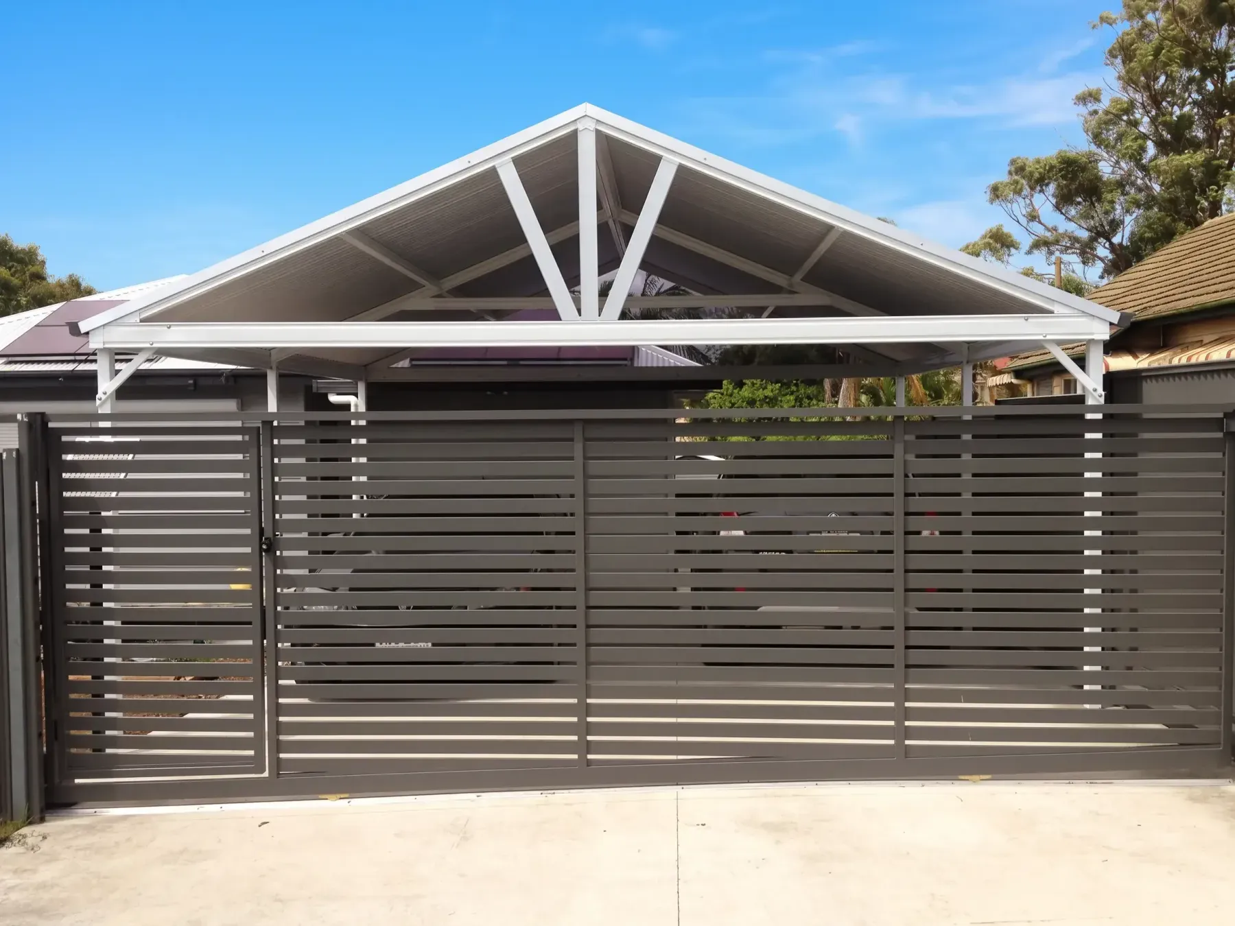 Gable carport with an exposed truss behind a slatted driveway gate