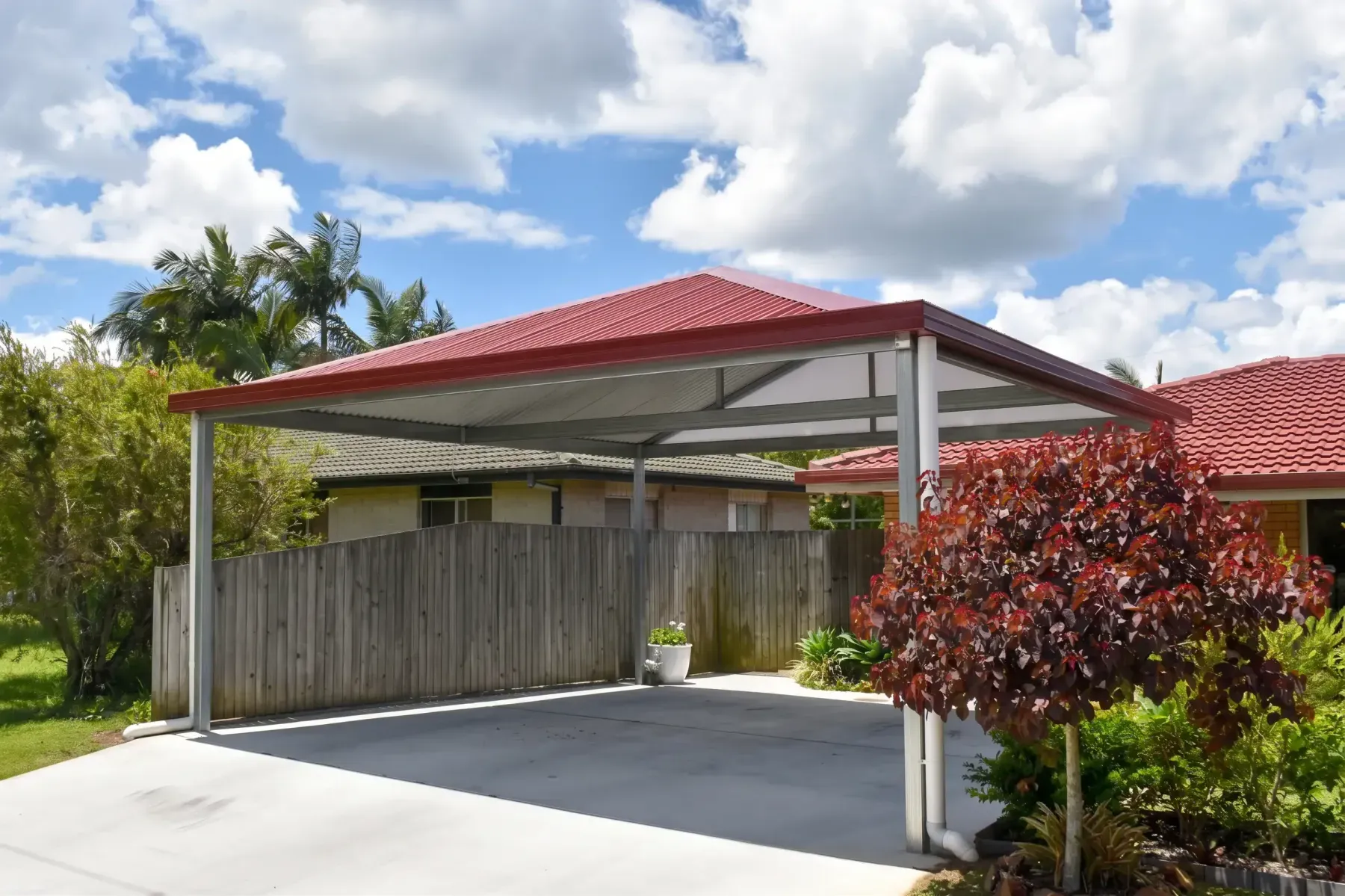 Gable carport with a red roof beside a garden bed