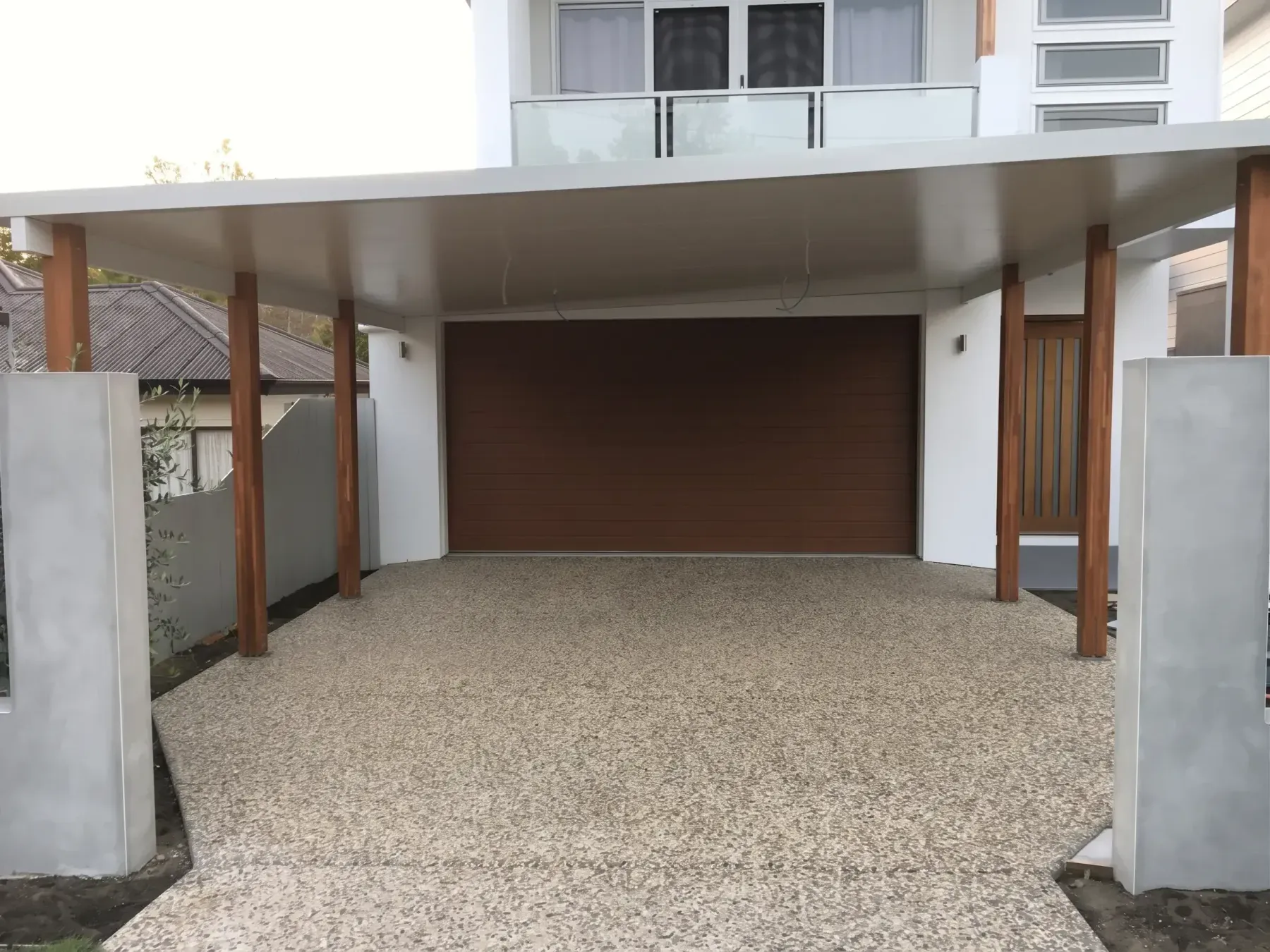 Flat roof carport with timber posts over an exposed aggregate driveway