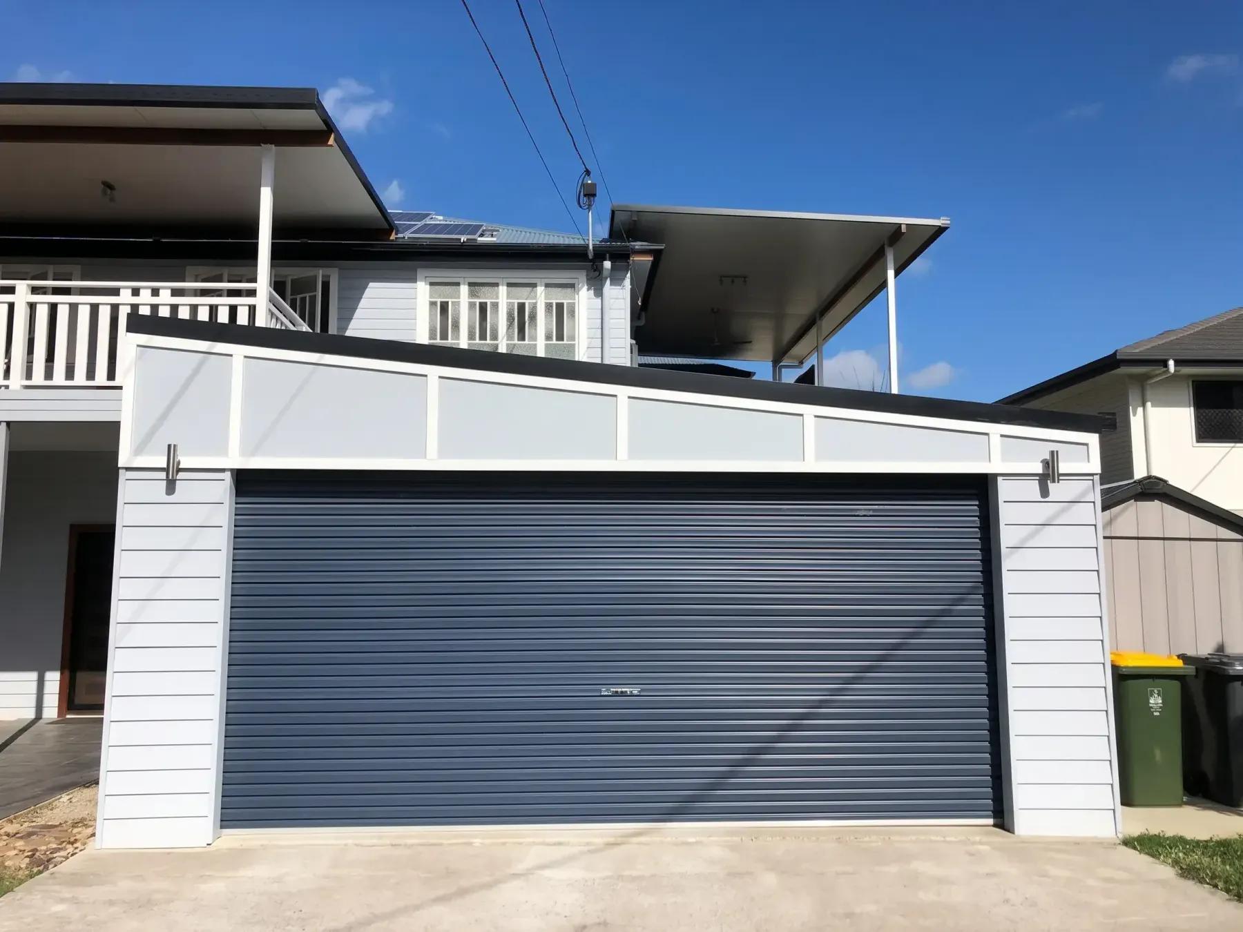 Weatherboard garage with a dark roller door under a two-storey home