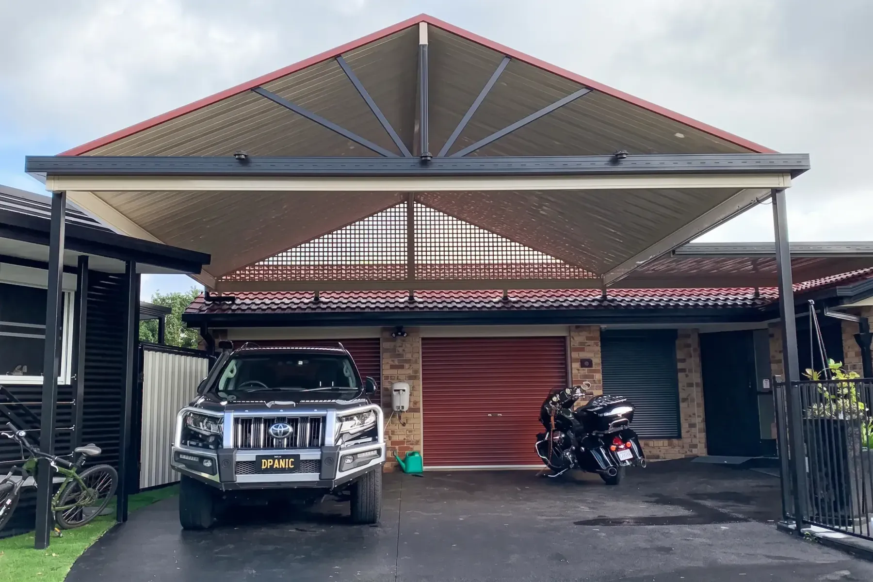 Gable carport over a 4WD and motorbike in front of a brick home