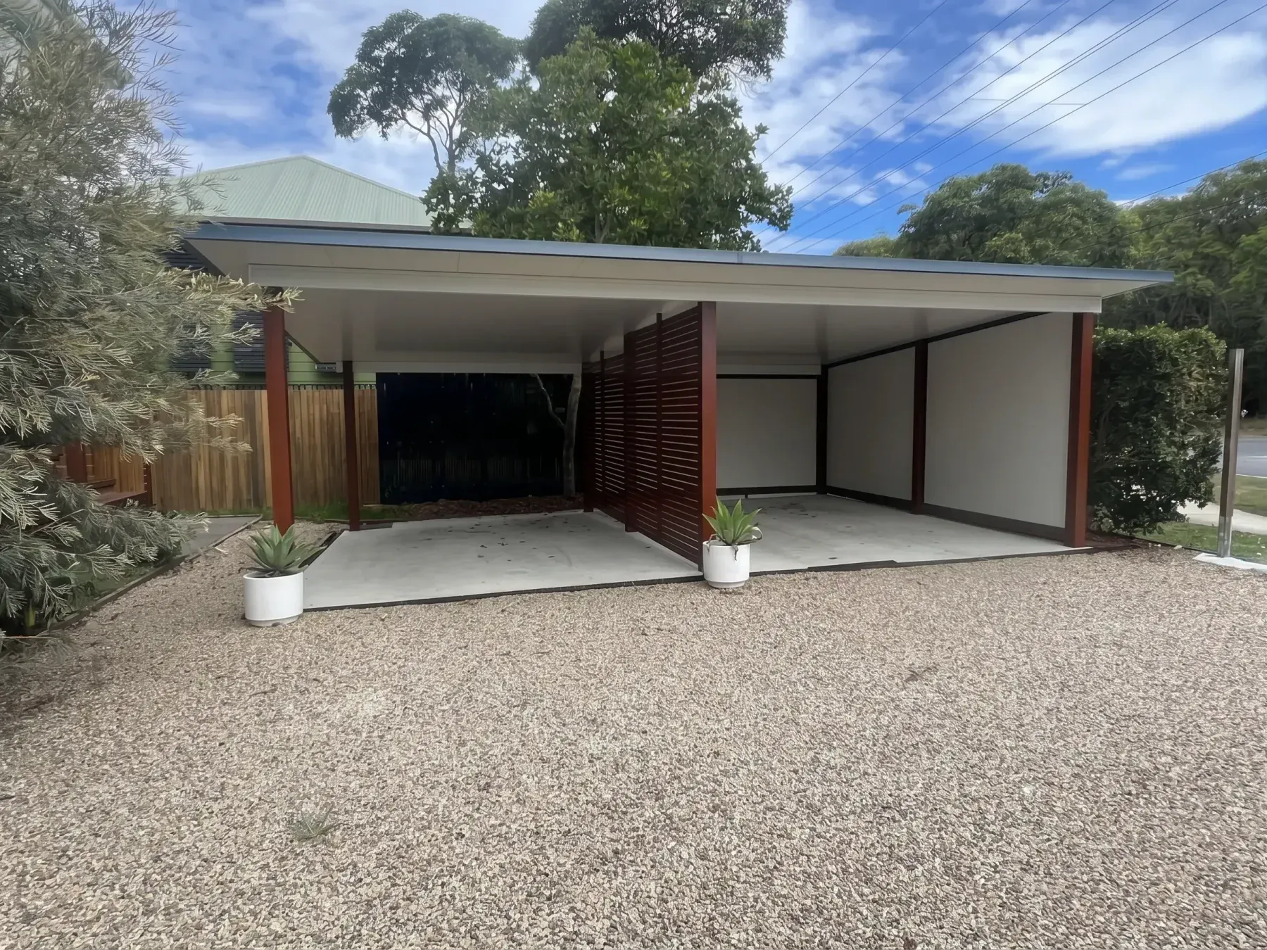 Wide carport over a gravel driveway with screens at the back