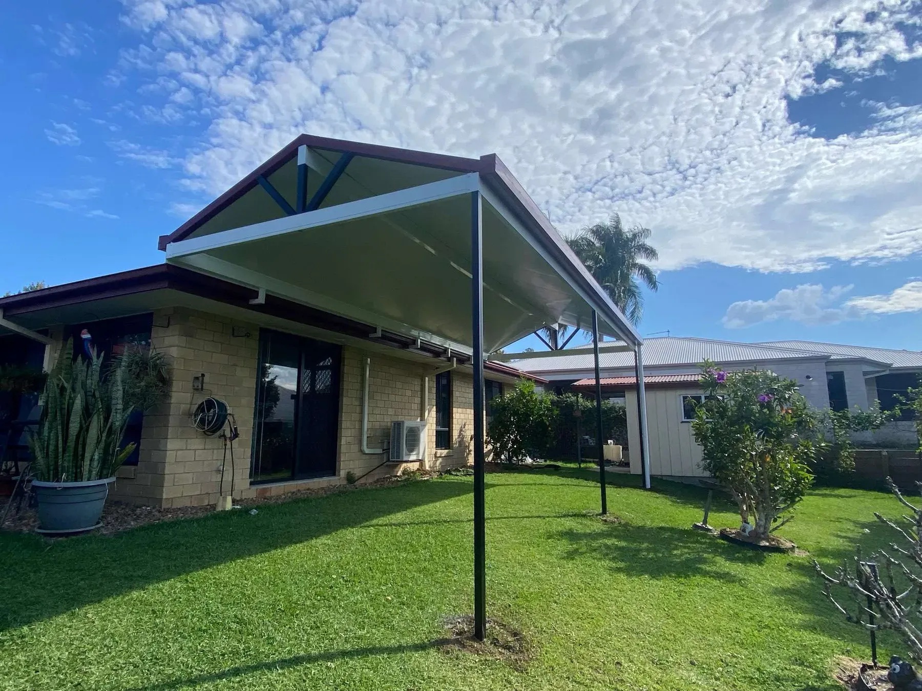 Gable roof frame over a lawn beside a brick home