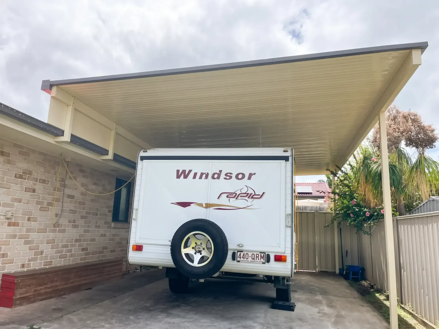 Carport over a caravan between a brick wall and a fence