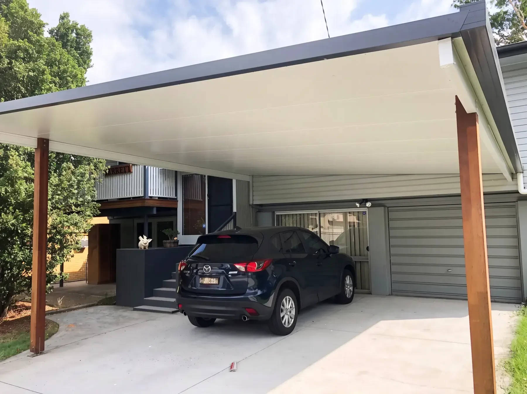 Carport with timber posts over an SUV in front of a garage