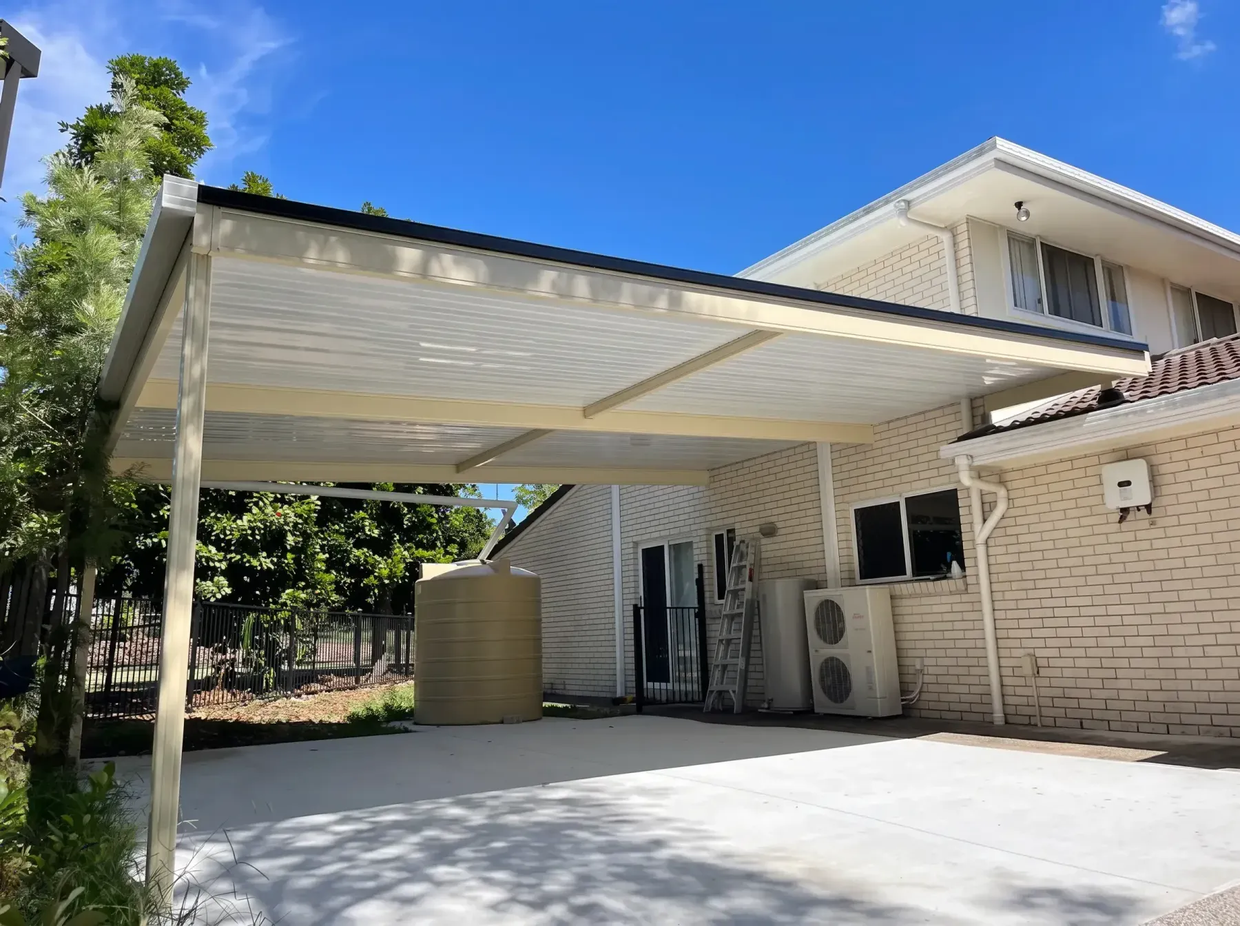 Flat roof carport over a concrete slab beside a two-storey home