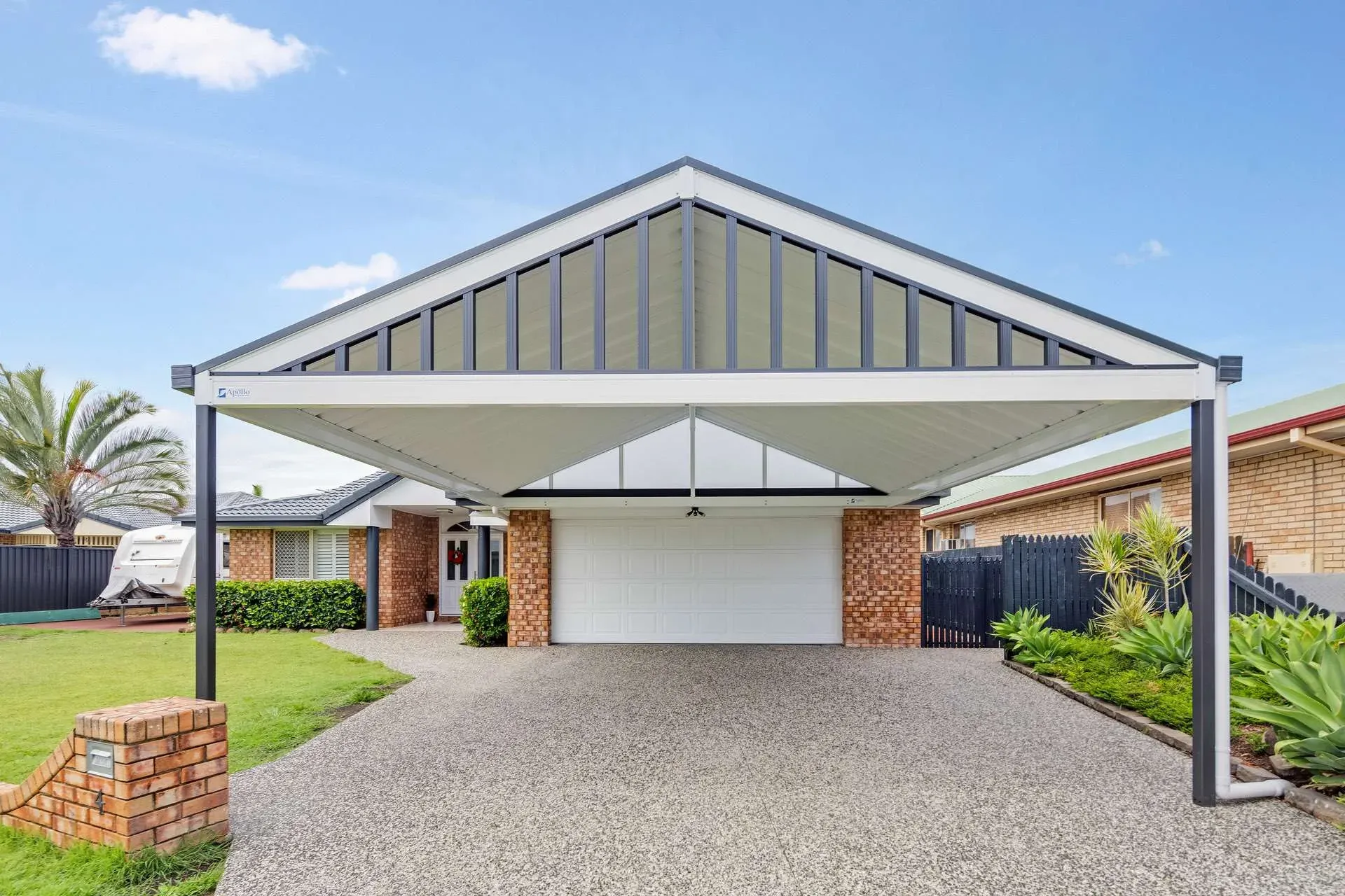 Wide double carport with a flat charcoal roof over a concrete driveway